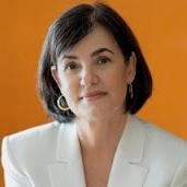 headshot of a woman with shoulder-length dark hair wearing a white blazer against an orange background