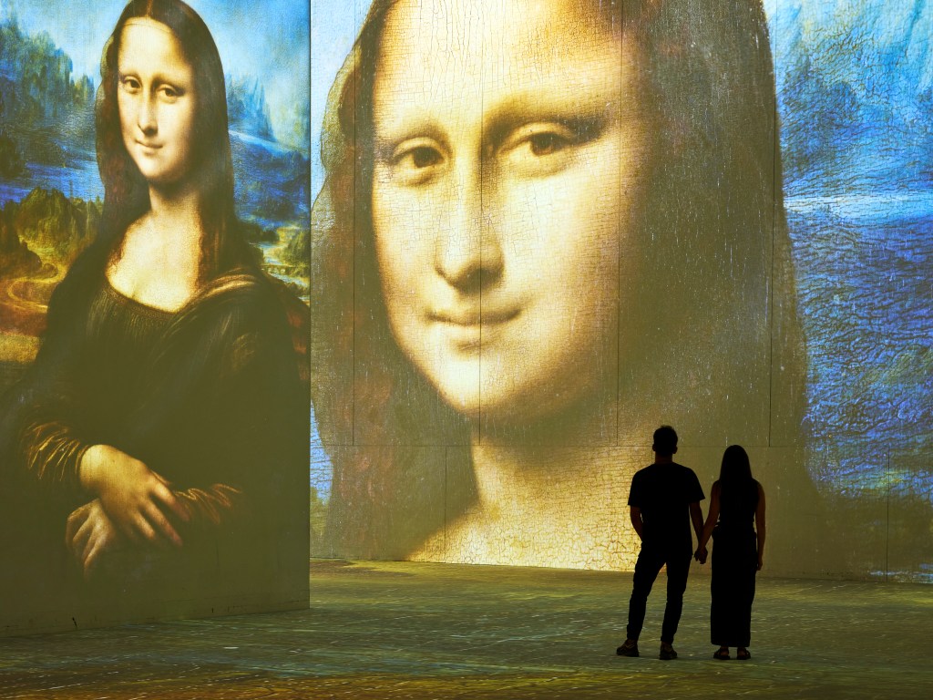 two silhouettes stand in front of wall-sized projections of the Mona Lisa