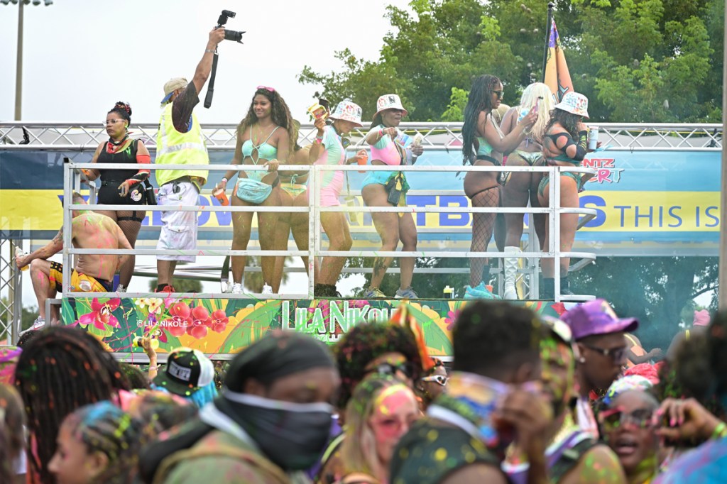 a group of people in festival outfits dance on a platform above other attendees