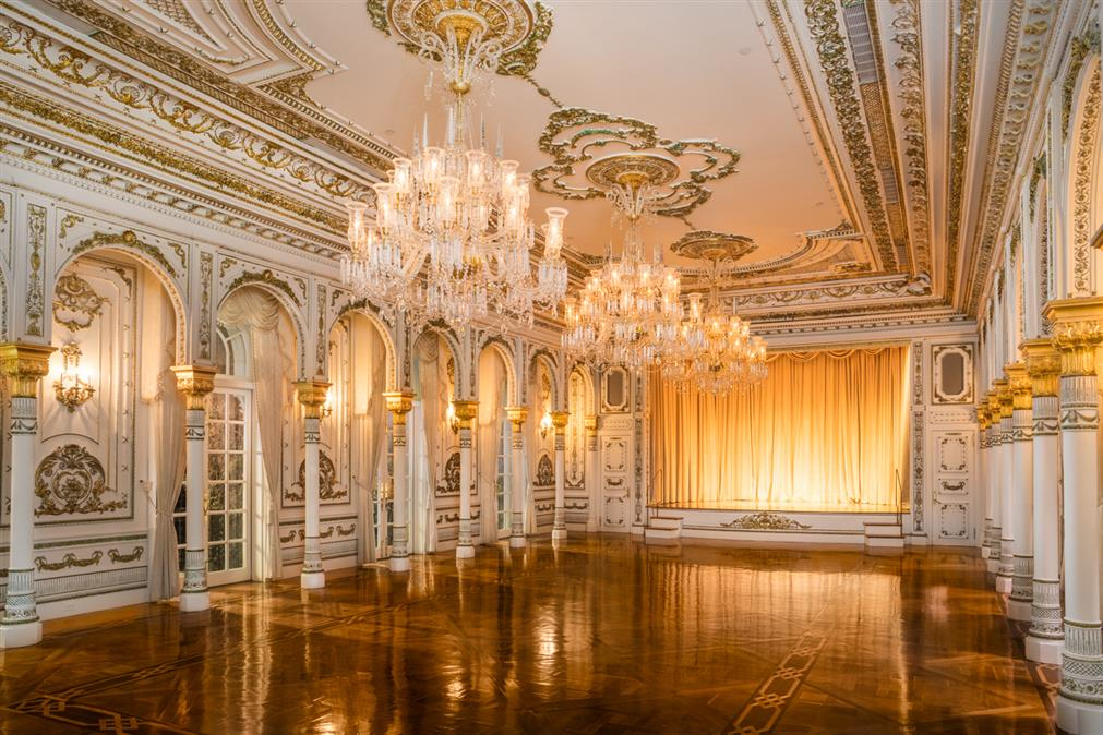 a wooden floor ballroom is surrounded by white walls with gold accents and ornate chandeliers