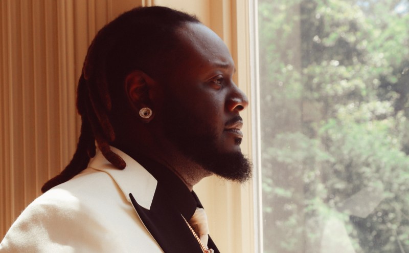 profile view of singer T-Pain looks out a window in a suit