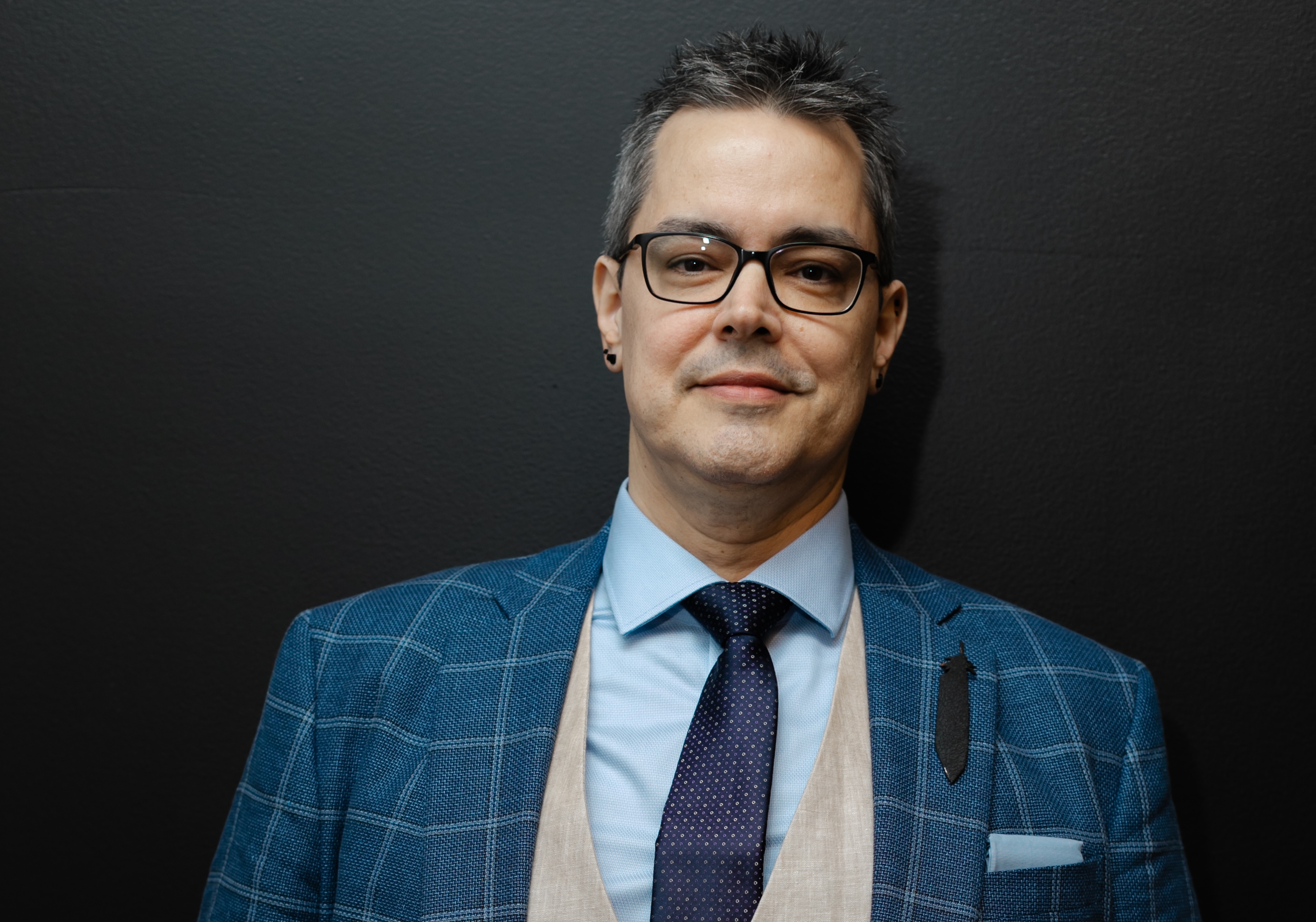 photo of author Aaron John Curtis from the shoulders up, wearing a suit and tie and standing in front of a black backdrop