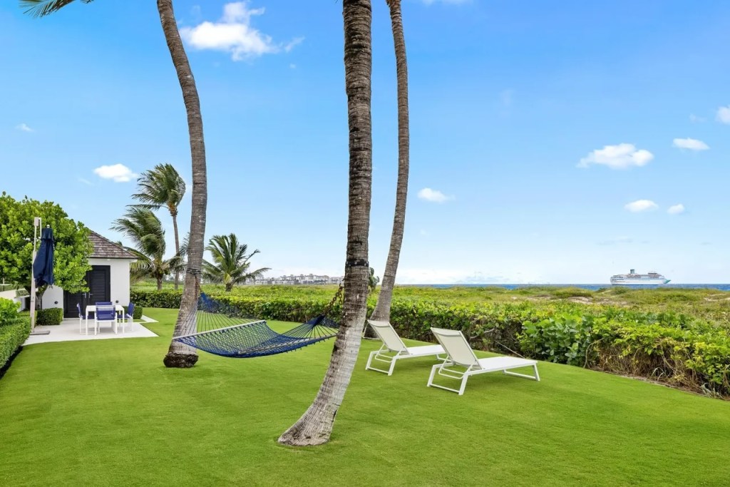 lawn chairs and a hammock rest near the edge of a lush backyard overlooking the beach
