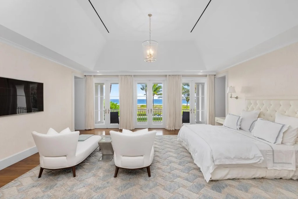 a pair of chaise lounge chairs sit at the foot of a large bed in an all-white bedroom