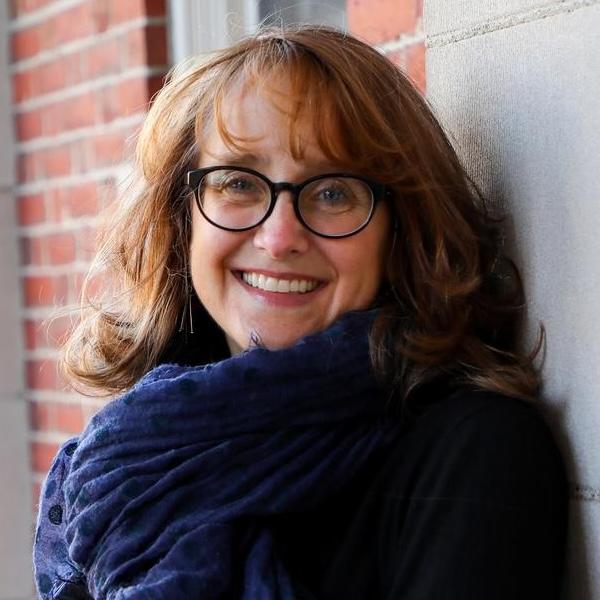 headshot of a smiling, bespectacled woman with red hair wearing a navy blue wool scarf