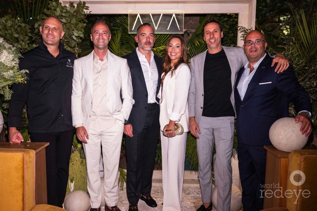 Photo of six people in suits posing at a restaurant. Above their heads is a sign reading, "AVA"