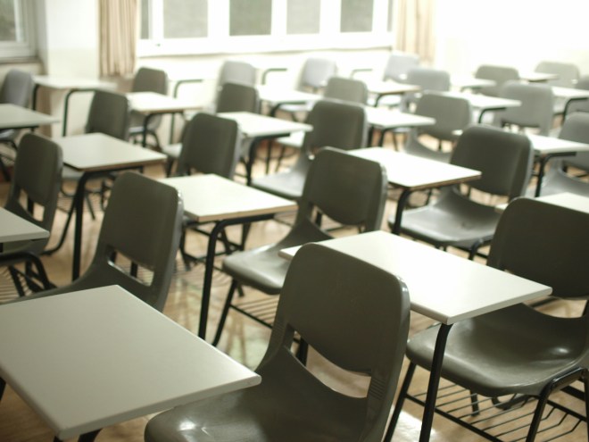 An empty classroom with rows of while desks and pale green chairs.