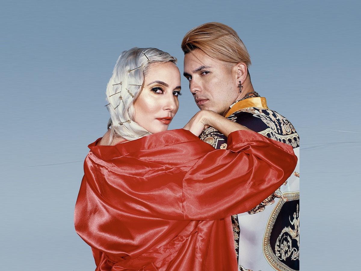 A woman and a man posing for the camera against a light blue background.