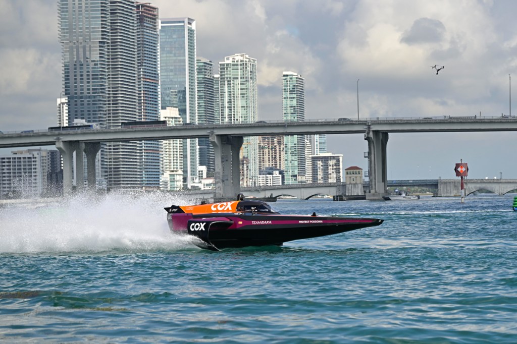 photo of a magenta and orange powerboat skimming over the water in front of the Miami skyline and a bridge