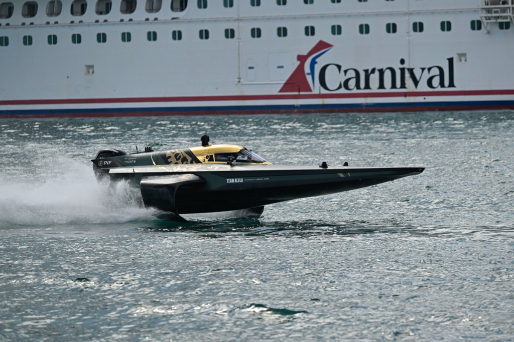photo of a green and gold powerboat reading "Team Alula" skimming over the ocean in front of a Carnival cruise ship