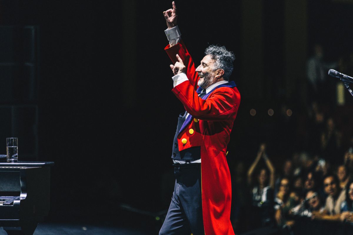 A singer on stage in front of a crowd raising his hand.