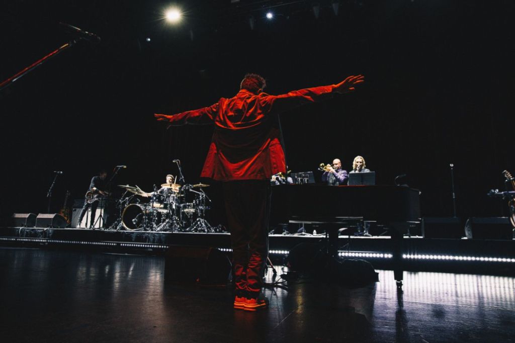 A singer on stage in front of a crowd raising his hand.