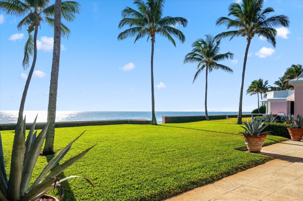 A manicured grass lawn dotted with tall palm trees overlooks the Atlantic Ocean's sun-lit waters