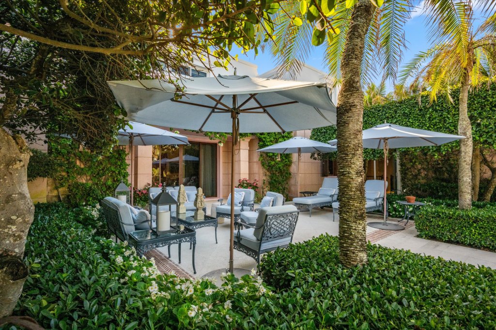 several ornate patio chairs sit in a lushly lined outdoor gathering area just outside the home