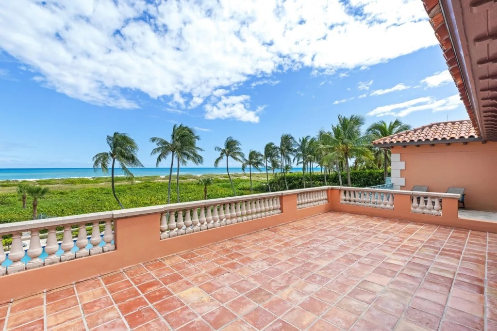 a Mediterranean-style deck overlooks a backyard pool, with palm trees and the Atlantic Ocean in the background