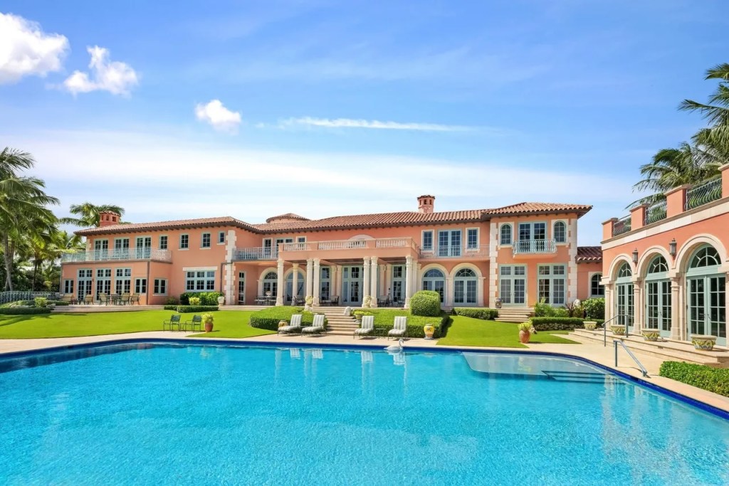 a massive resort-style pool spans the foreground with a pink mansion stretching the length of the frame