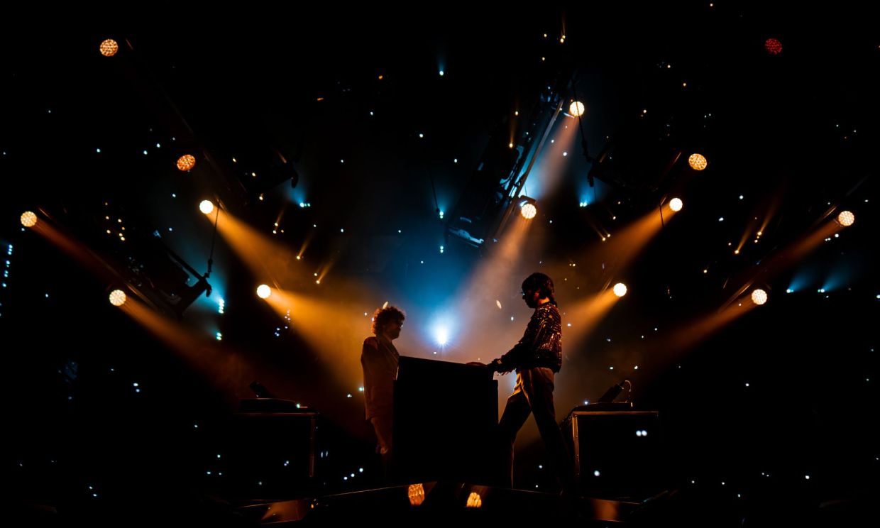 Photo of two men on stage playing synthesizers.
