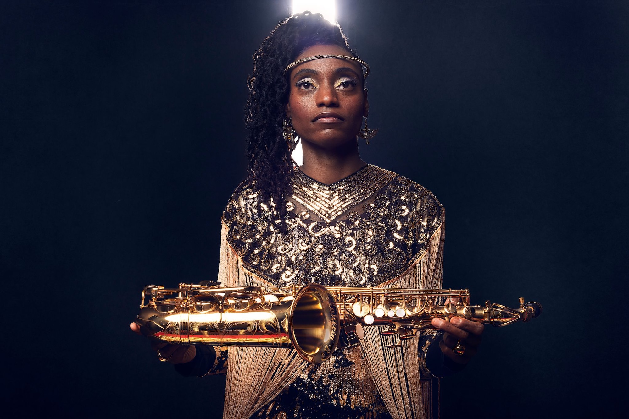 Photo of a woman wearing a golden dress and holding a saxophone.