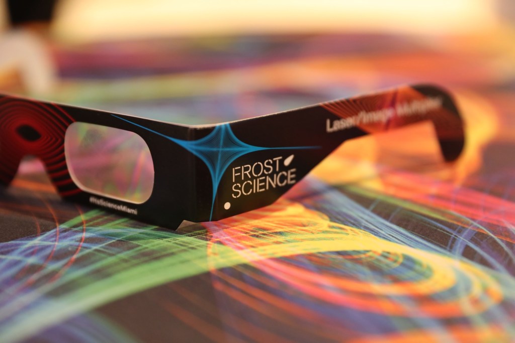 Close-up photo of 3D glasses on top of a surface with colorful spiral graphics. Text on the 3D glasses reads, "Frost Science."