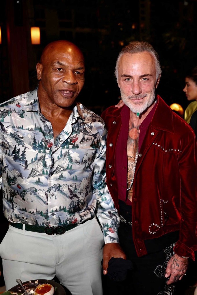 photo of boxer Mike Tyson in a patterned silk button-down long-sleeved shirt and slacks posing next to entrepreneur Gianluca Vacchi in a red bedazzled jacket without a shirt underneath