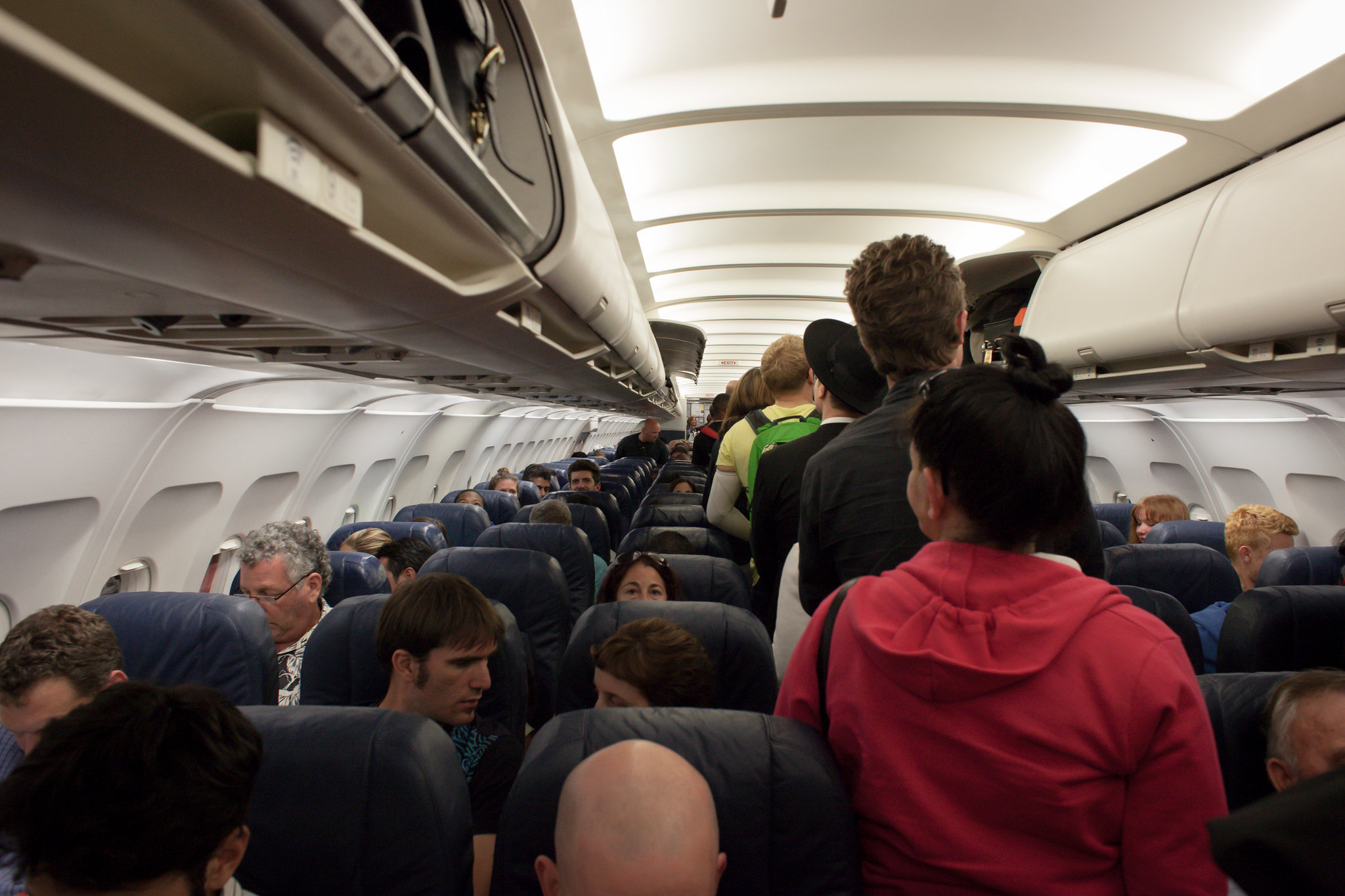 passengers sit in rows on either side of people waiting in a line to take their seats