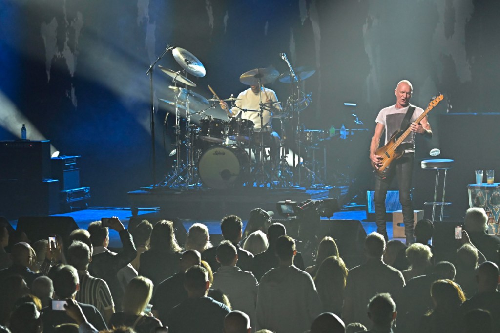 A band performing in front of a crowd under blue lights.