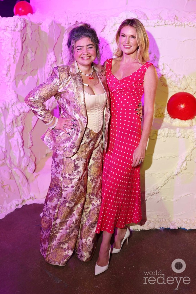 photo of two women posing in formalwear in front of a sculpture of a giant birthday cake