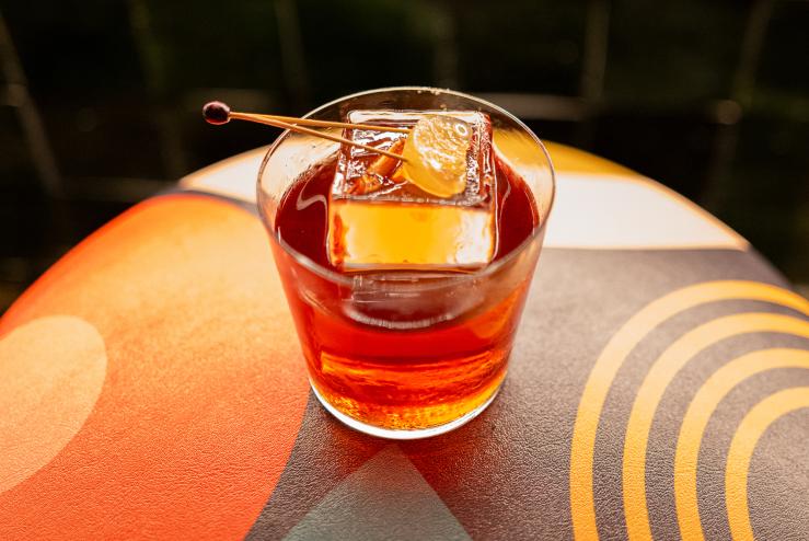 an orange cocktail in a glass with an ice cube on a futuristic orange table
