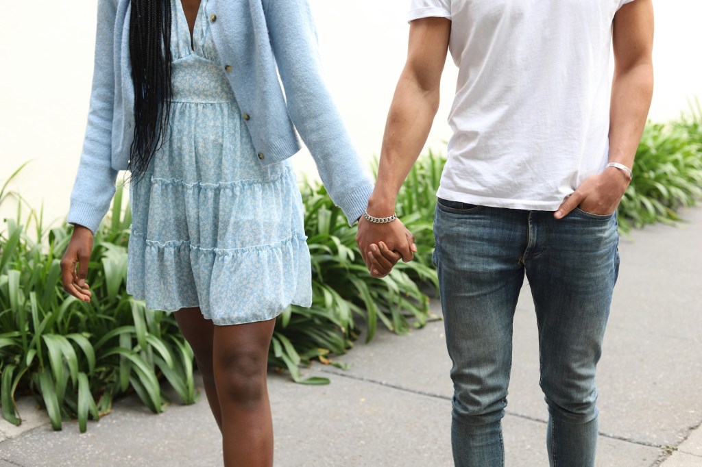 photo of a woman in a dress and cardigan and a man in a white T-shirt and jeans holding hands