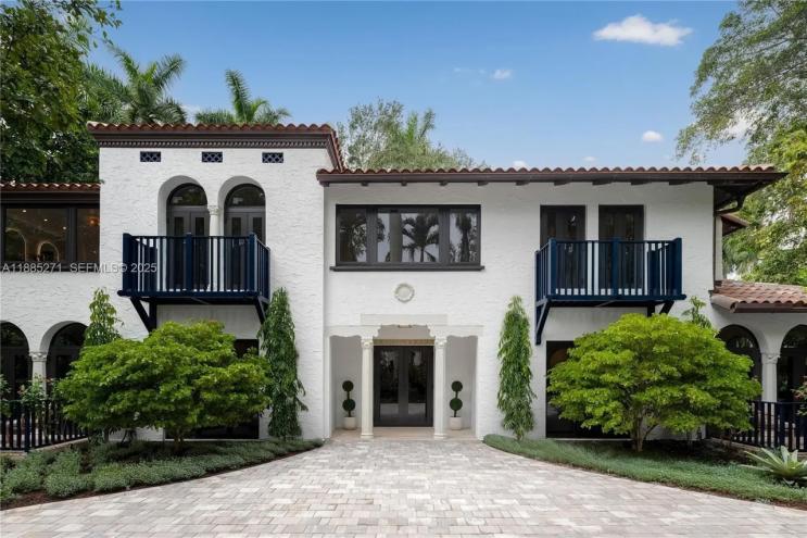 a white, Mediterranean-inspired mansion sits behind naturally manicured trees