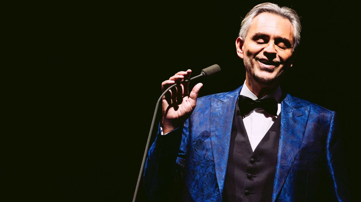 Photo of a man on stage holding a mic wearing a smoking