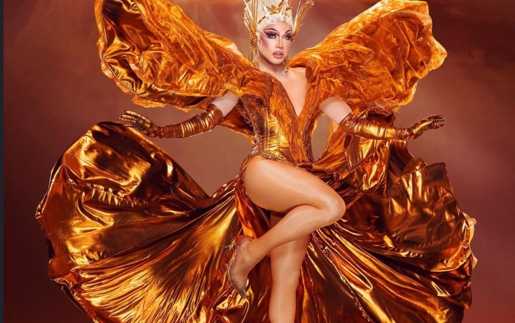 photo of a drag performer in a shiny silk ballgown with exaggerated shoulder protrusions and silk gloves