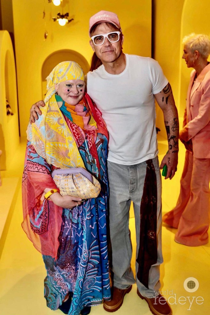 photo of designer Bethan Laura Wood posing with singer Robbie Williams inside a bright-yellow room