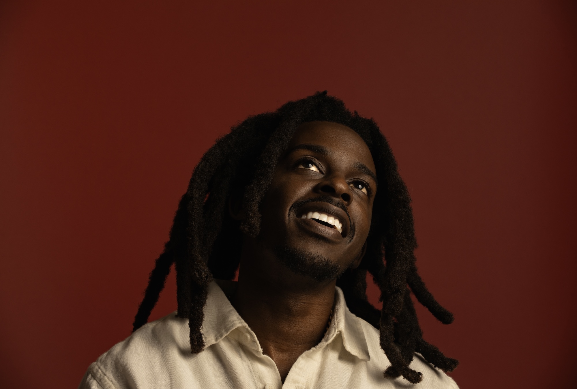 Photo of a man with dreadlocks smiling and looking up.