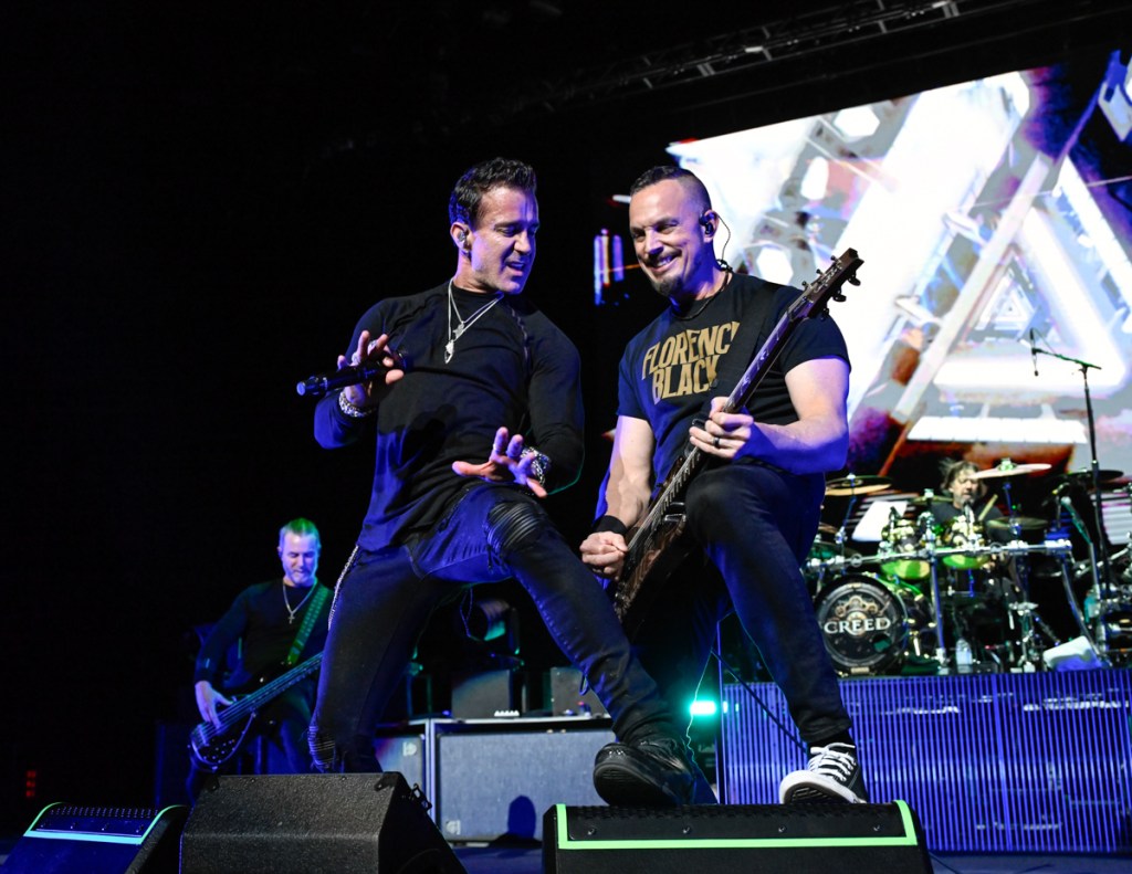 Photo of two men on stage wearing black, one is playing the guitar and the other one is holding a microphone. 