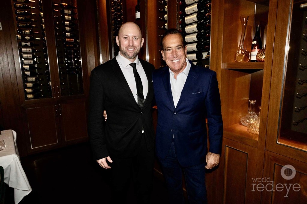 photo of two men posing together in suits inside a restaurant