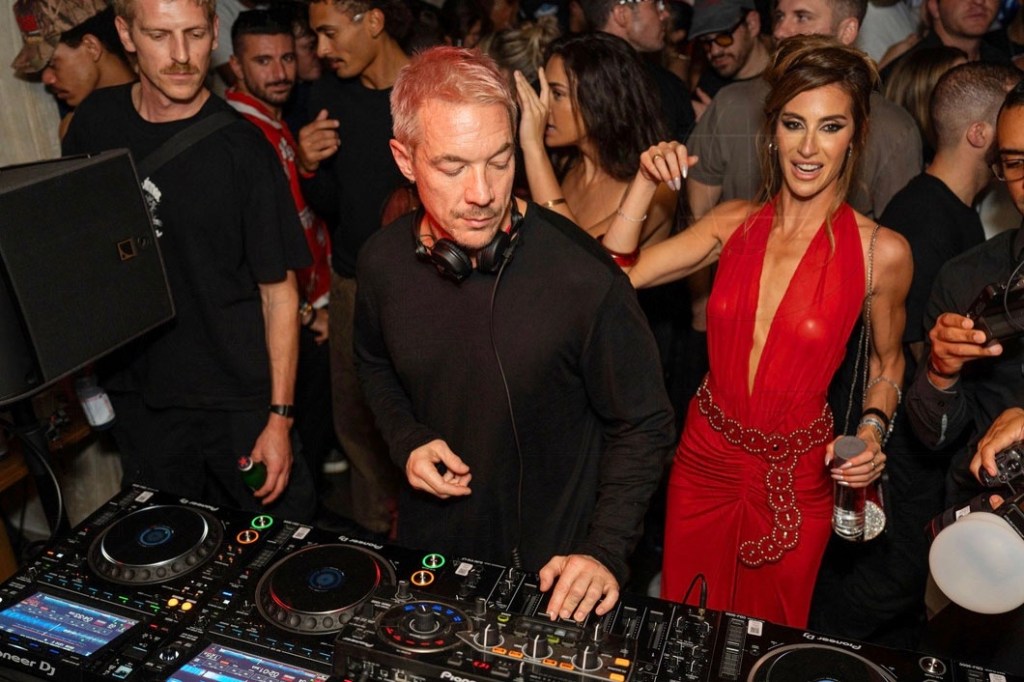 photo of Diplo performing behind a DJ booth with a crowd behind him
