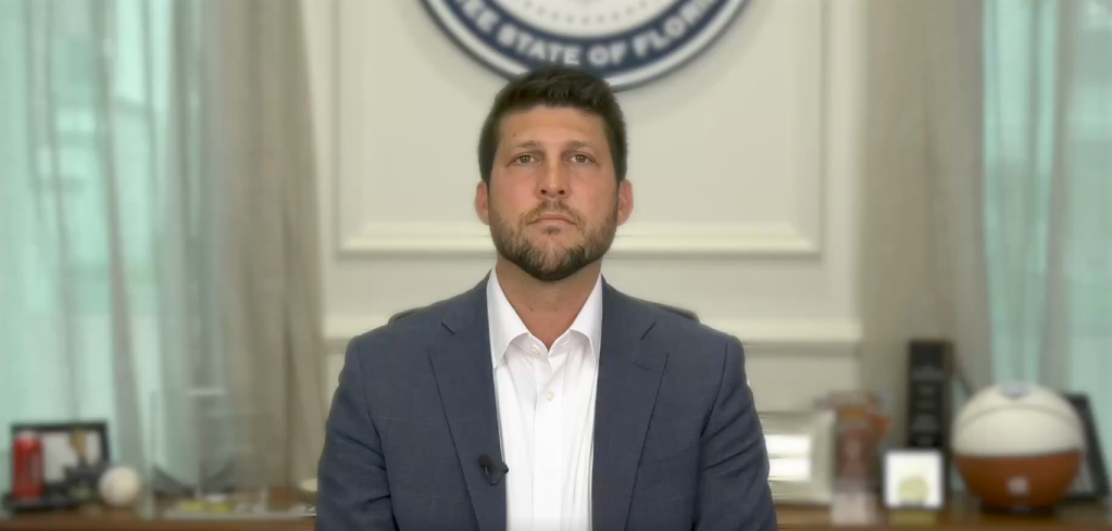 Florida Attorney General James Uthmeier speaks from his desk, donning a grey blazer and white shirt