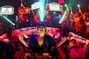 photo of DJ John Summit performing at a club with bottle girls holding up signs behind him