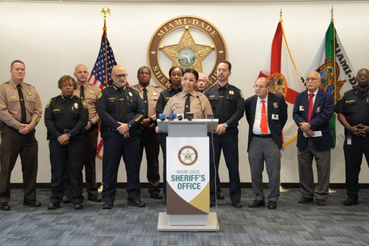 Miami-Dade Sheriff Rosie Cordero-Stutz speaks at a podium wearing her police uniform surrounded by Miami-Dade Sheriff's Office police officers and officers from the Miami Police Department.