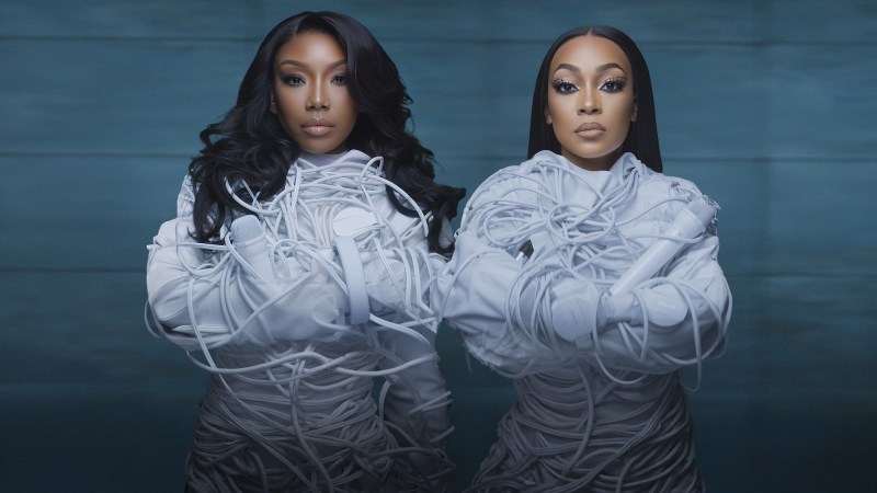 photo of singers Brandy and Monica wearing white straight jackets wrapped in white microphone and headphone wires
