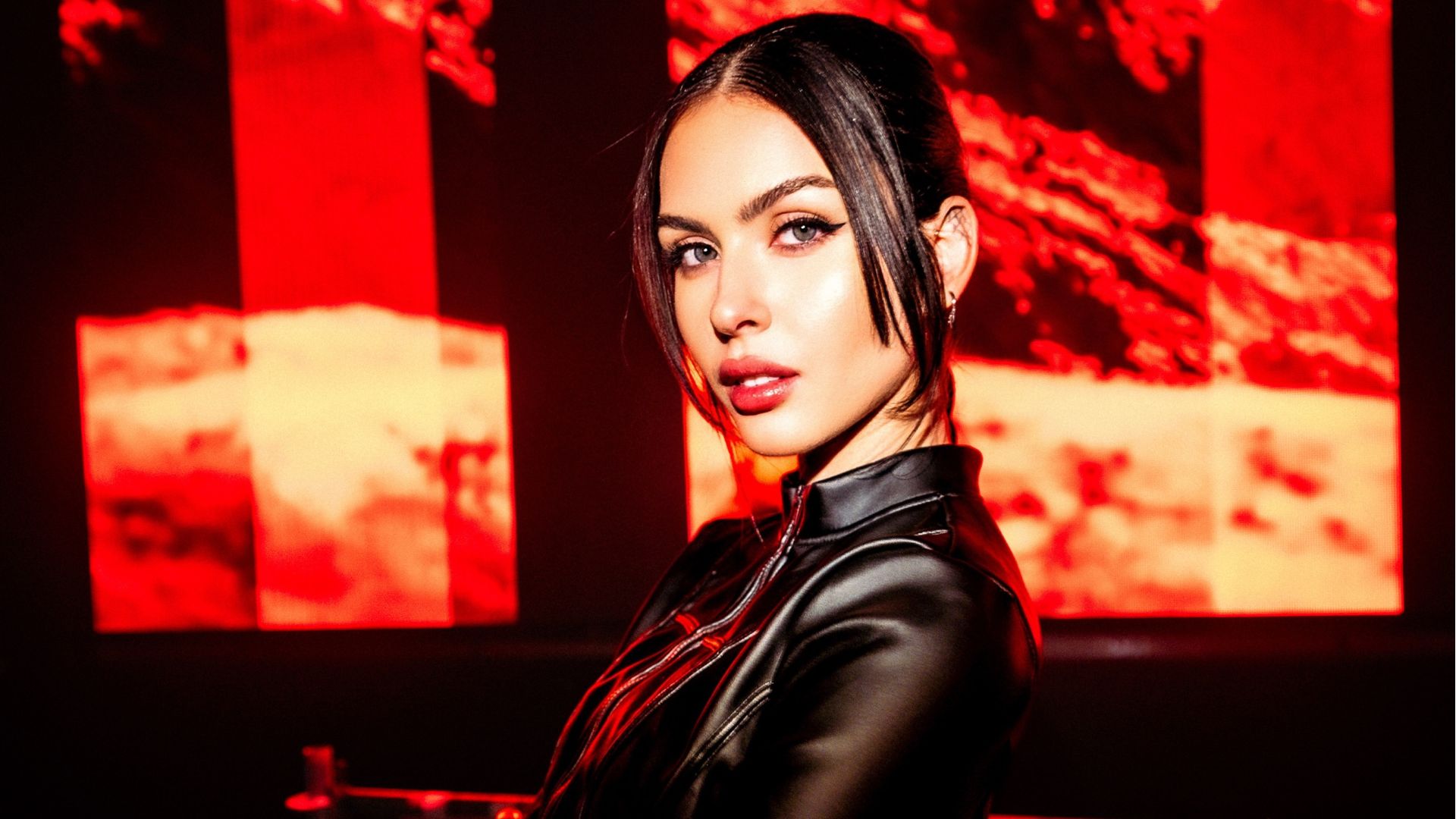 Photo of a woman wearing black against a red LED screen