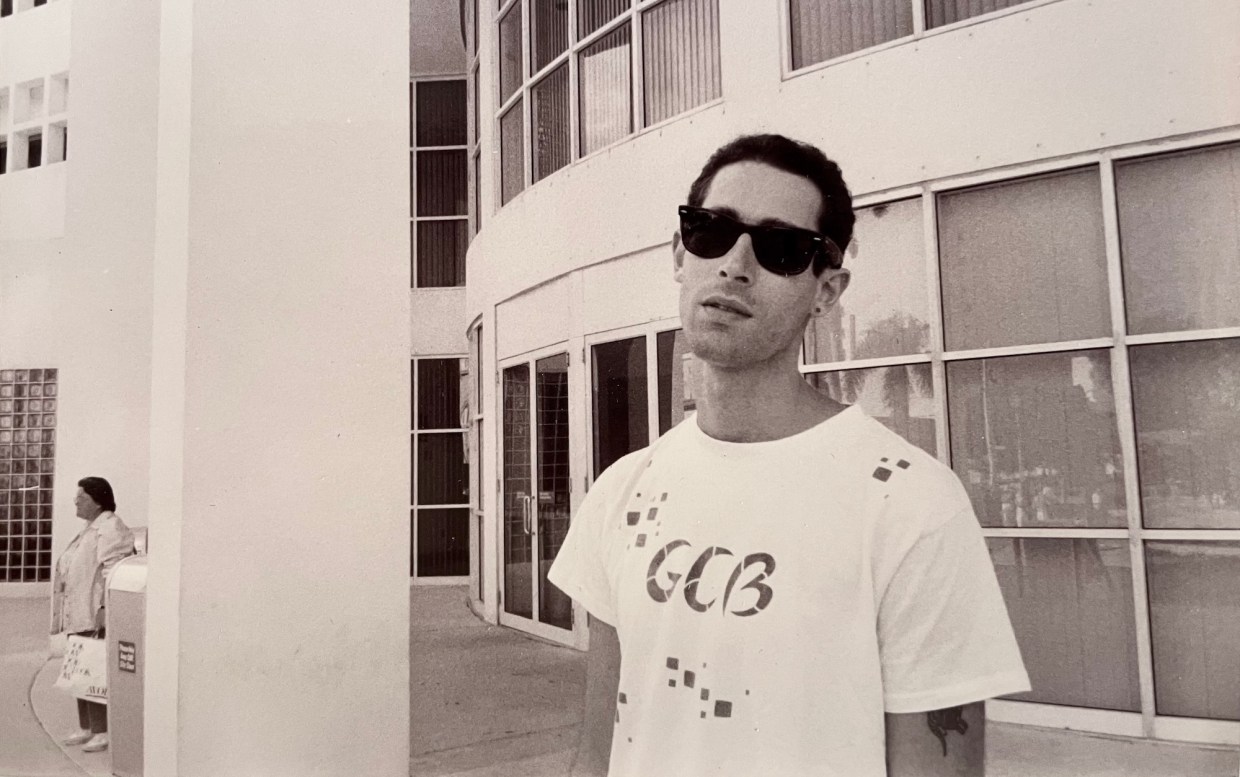 archival black-and-white photo of a young man in a T-shirt and Ray-Ban Wayfarer sunglasses giving the photographer the side-eye