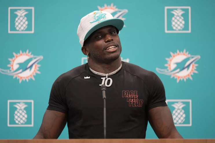 Tyreek Hill speaks at a press conference weating a white Dolphins hat and a fitted black t-shirt and a large silver chain.