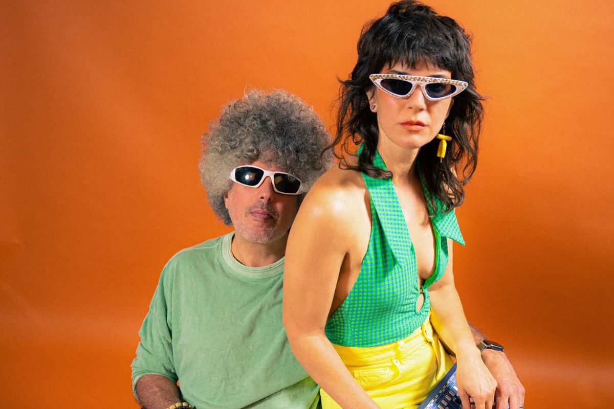 Photo of a woman sitting on a man's lap against an orange backdrop