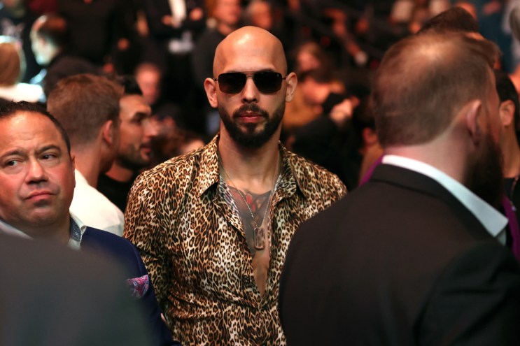 A bald man wearing sunglasses and a leopard print button down shirt.