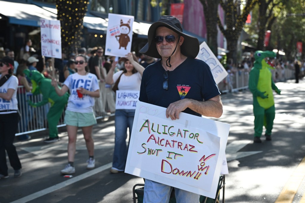 photo of a man at a parade holding a sign reading, "Alligator Alcatraz, shut it down! Now!'
