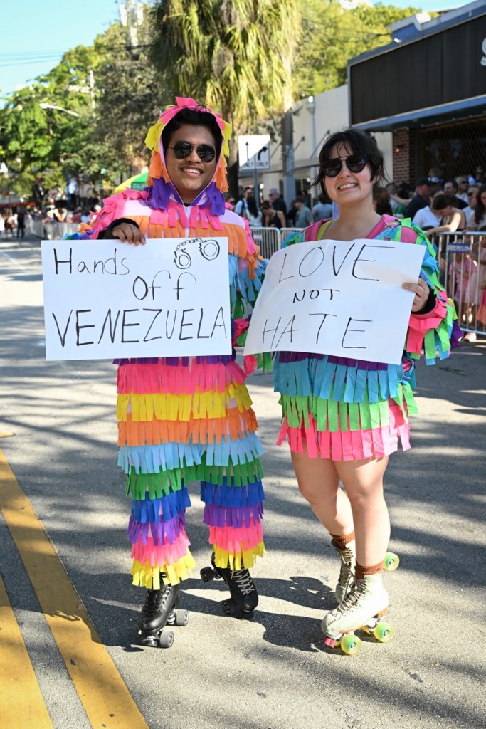 photo of two people wearing fringed, colorful costumes and rollerblades. One holds a sign reading, "Hands off Venezuela." The other holds a sign reading, "love not hate"