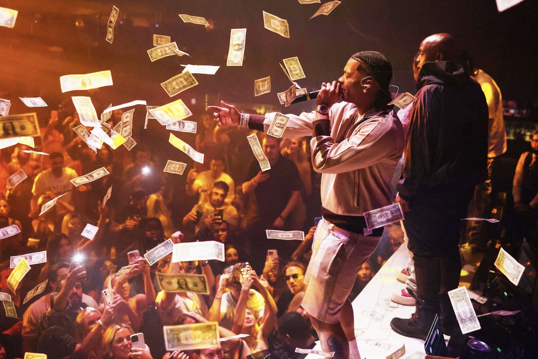 photo of rapper Lil Baby performing onstage at a club as dollar bills rain down around him