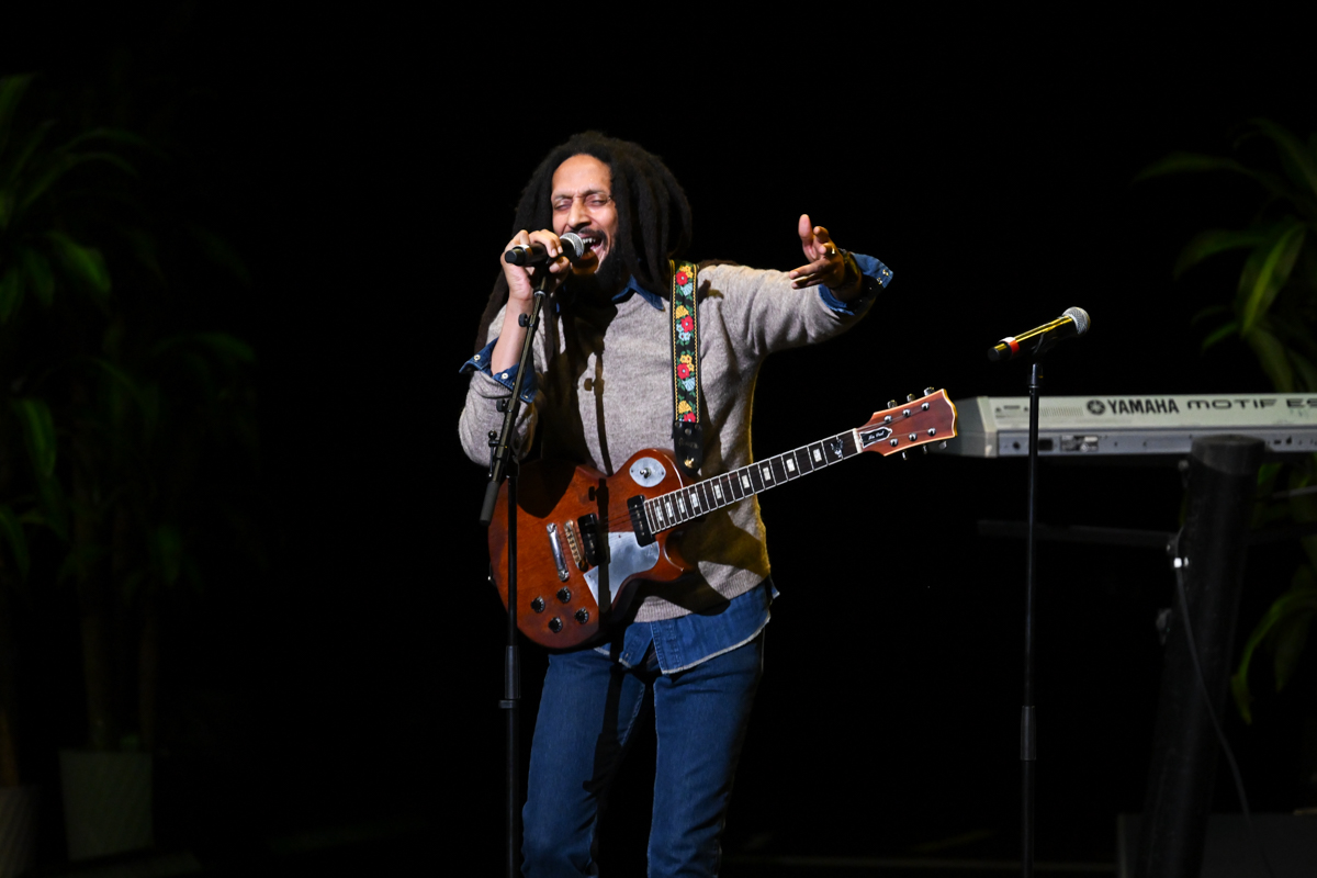 a man with dreadlocks on stage singing and holding a guitar.